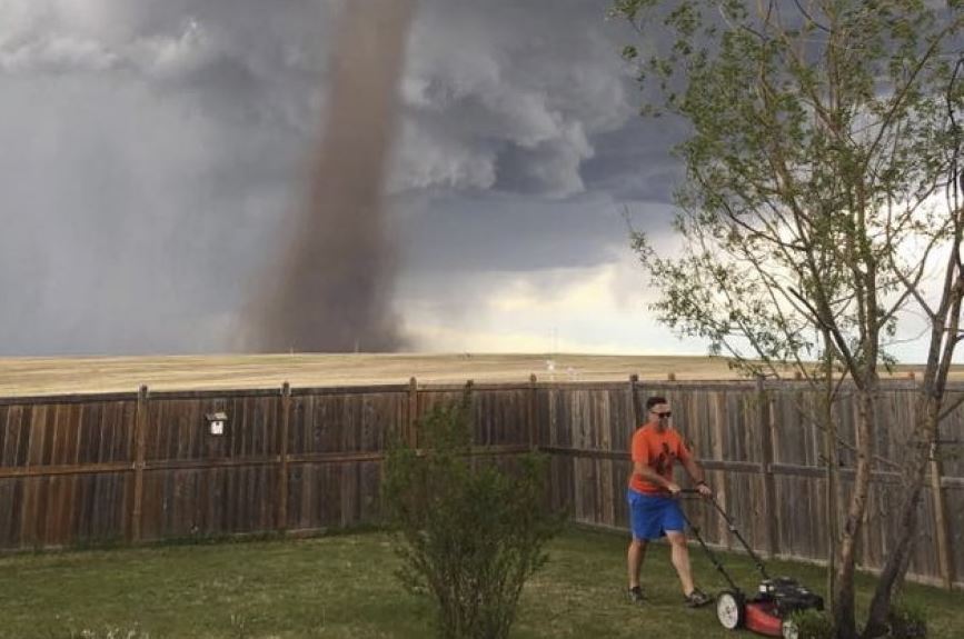 Taglia l’erba con il tornado alle spalle: la foto diventa virale