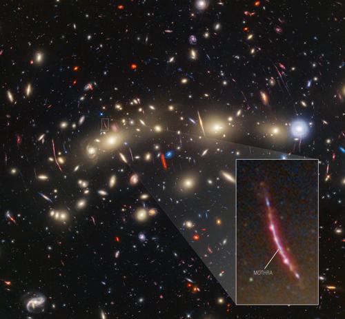 Un campo di galassie sullo sfondo nero dello spazio. Al centro, che si estende da sinistra a destra, c'è una collezione di decine di galassie a spirale e ellittiche giallastre che formano un ammasso di galassie in primo piano. Tra di esse ci sono caratteristiche lineari distorte create quando la luce di una galassia di sfondo viene piegata e ingrandita attraverso la lente gravitazionale. A sinistra al centro, un esempio particolarmente prominente si estende verticalmente per circa tre volte la lunghezza di una galassia vicina. È delimitato da un riquadro bianco, e una cuneo leggermente ombreggiato porta a una vista ingrandita in basso a destra. La caratteristica lineare è rossiccia e si curva dolcemente. È punteggiata da circa una mezza dozzina di ammassi luminosi. Un punto simile vicino al centro della caratteristica è etichettato come 