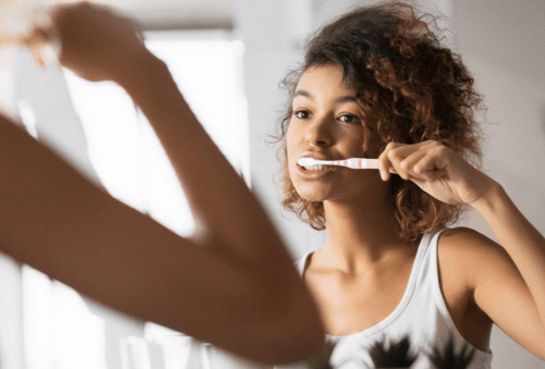 Giovane donna allegra che si diverte a spazzolare i denti allo specchio.