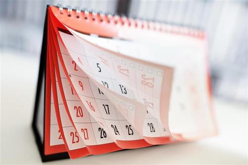 Una foto di un calendario rosso e bianco su un tavolo. Le pagine del calendario si stanno sfogliando come se fossero spinte dal vento, suggerendo che il tempo sta passando.