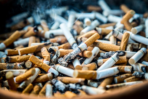 Mozziconi di sigaretta con cenere nel posacenere, area fumatori / vita non salutare