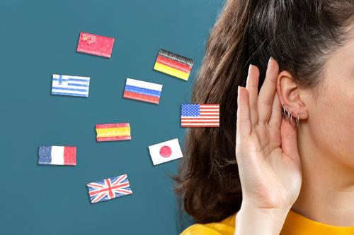 disegni di bandiere di diversi paesi accanto alla mano di una persona che tiene l'orecchio per indicare l'ascolto di lingue diverse