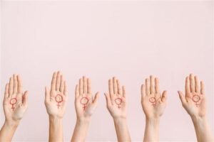 Una foto di sei mani femminili rivolte verso il palmo in avanti su uno sfondo rosa. Ogni mano ha il simbolo femminile dipinto sui palmi.