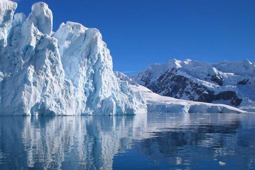 Grande ghiacciaio, con cielo azzurro sullo sfondo e acqua in primo piano.