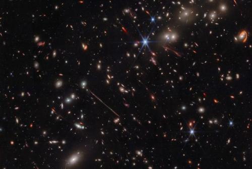 La composizione mostra molte galassie su uno sfondo nero. Alcuni oggetti più vicini sono gialli ed ellittici e ci sono alcune linee rosse. Queste sono galassie estremamente gravitazionalmente lente che il cluster El Gordo sta deformando e ingrandendo.