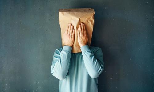 Persona con una borsa di carta sulla testa e le mani alzate verso il viso come cercando di bloccare ogni suono o vista