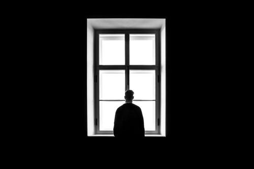 silhouette di un uomo che sta in piedi da solo di fronte a una finestra, immagine in bianco e nero