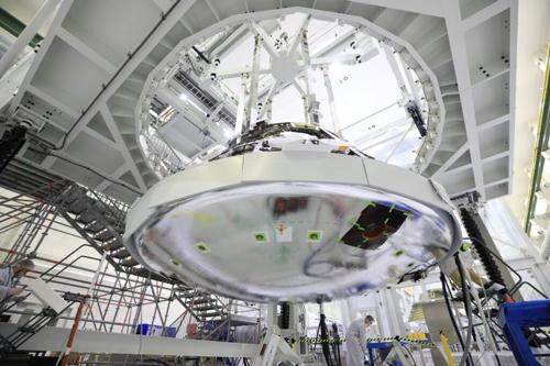 Viene mostrata la parte inferiore metallica della capsula Artemis Orion che porterà gli astronauti sulla Luna. Orion è sospeso e un lavoratore si trova sotto.