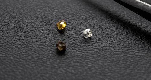 Tre piccoli diamanti posizionati su una superficie nera - uno è giallo, uno è incolore e uno è marrone scuro/grigio.