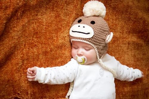 bambino che dorme con ciuccio indossando un cappello da scimmia lavorato a maglia