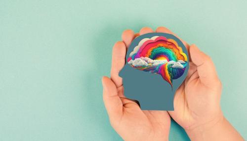 mani che tengono la sagoma di una testa umana con un cervello dai colori dell'arcobaleno su sfondo azzurro chiaro