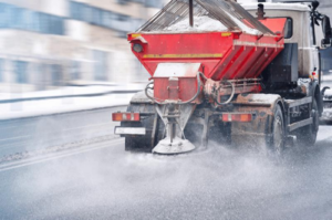 Autocarro spargisale per la manutenzione stradale e autostradale che sparge sale antigelo sulla strada in inverno. Spargimento di sale. Autocarro spazzaneve che rimuove la neve e sparge sale su una strada cittadina innevata durante una tempesta di neve