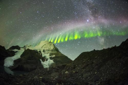 fenomeno STEVE di colore malva e recinzione verde nel cielo sopra una montagna innevata