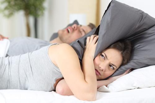 una donna sembra poco impressionata tenendo un cuscino sulle orecchie mentre il partner russa nel letto accanto a lei