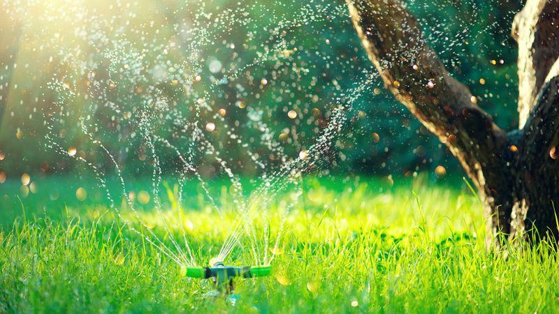 Un sistema di irrigazione a spruzzo in un giardino che spruzza acqua da tre rubinetti rotanti