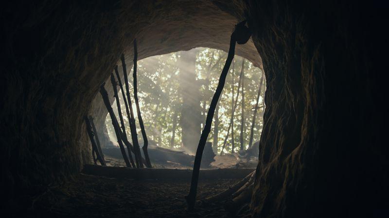 Scatto fatto dalla grotta verso la foresta preistorica. Luogo di vita del Neanderthal con attrezzi di pietra primordiali e bastoni.