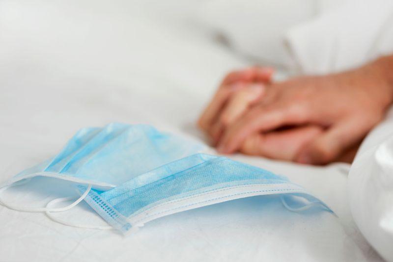 Maschere chirurgiche su un letto con le mani intrecciate di due persone sullo sfondo