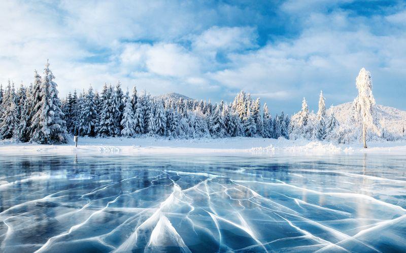 Crepe sulla superficie del ghiaccio blu. Lago ghiacciato nelle montagne invernali. Sta nevicando. Le colline di pini. Carpati Ucraina Europa.