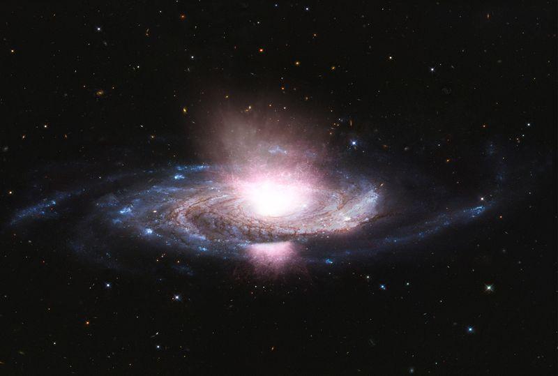 Vista laterale di una galassia con bracci a spirale di stelle blu brillanti separati da bande scure di polvere interstellare. Il centro attivo della galassia sta emettendo un forte vento di gas in tutte le direzioni, mostrato come striature bianco-giallastre. Un ingrandimento mostra che il vento proviene da un disco vorticoso di gas, illuminato di arancione e giallo, che circonda un buco nero supermassiccio.