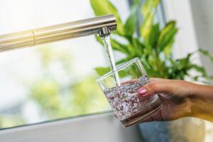mano che tiene un bicchiere che si riempie d'acqua da un rubinetto