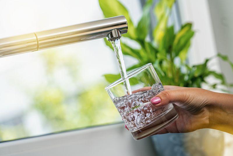 mano che tiene un bicchiere che si riempie d'acqua da un rubinetto