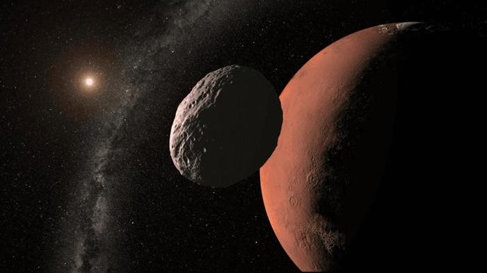 Rappresentazione artistica di un asteroide a forma di patata con Marte che appare grande dietro di esso.