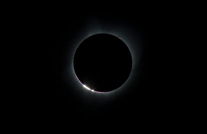 Una foto di un'eclissi solare e una serie di punti luminosi simili a perline sono visibili sul bordo della Luna mentre copre quasi il Sole