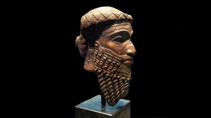 Una foto di profilo di una testa di bronzo di un sovrano accadico sconosciuto. La testa appartiene a un uomo e mostra la sua lunga barba arricciata e una fascia o corona stilizzata sulla fronte.