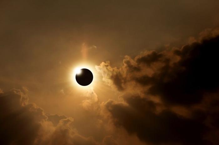 eclissi totale del sole contro un cielo arancione scuro con nuvole nere