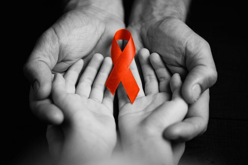 Consapevolezza dell'HIV nastro rosso tenuto nelle mani di un bambino, che sono tenute nelle mani di un adulto. Tutto in bianco e nero tranne il nastro.