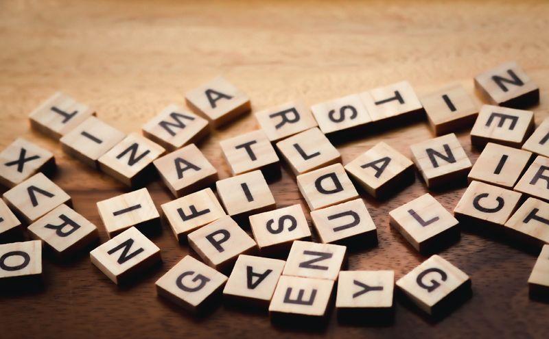 scattered wooden tiles with different letters of the alphabet on a wooden table, some of the letters are upside down and they're not in any order