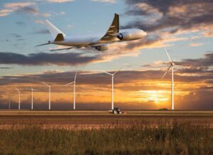 Un aereo decolla sopra un campo agricolo e generatori eolici