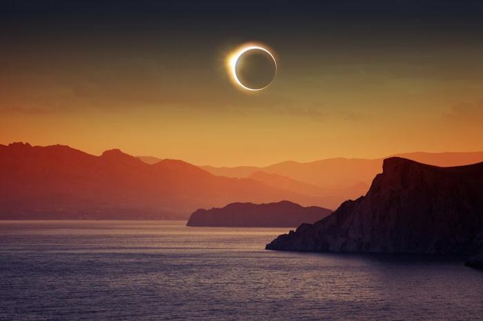 Eclissi solare su un cielo giallo-arancione, scogli e mare