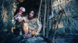 Uomo neolitico cavernicolo nell'età della pietra che indossa pelle animale tiene carne e osso vicino all'ingresso della caverna.