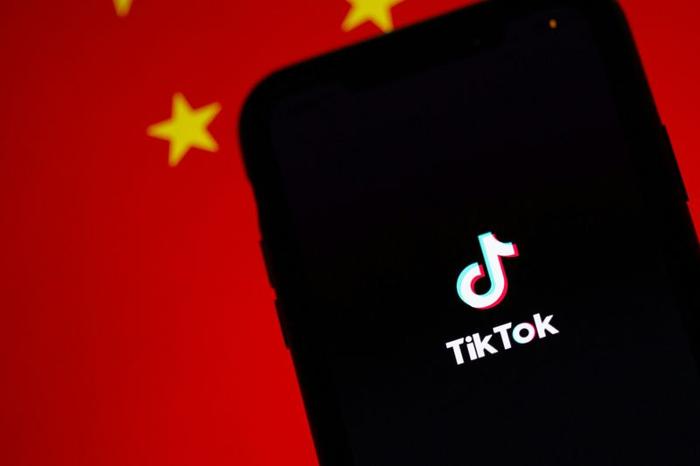 Uno smartphone che mostra l'applicazione di social media TikTok di fronte a una bandiera rossa della Cina