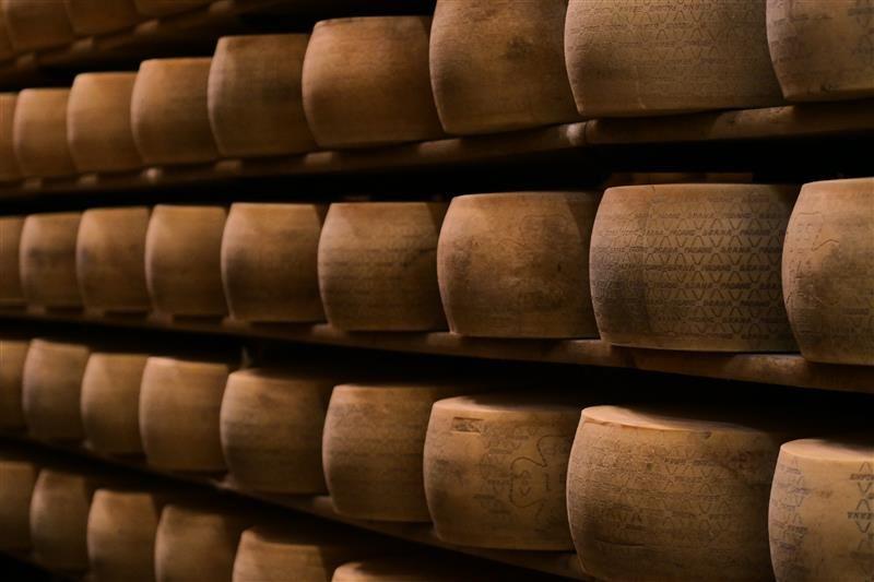 File di ruote di formaggio caricate su scaffali. L'immagine mostra gli scaffali che si estendono oltre il telaio e sono impilati almeno cinque scaffali in totale.