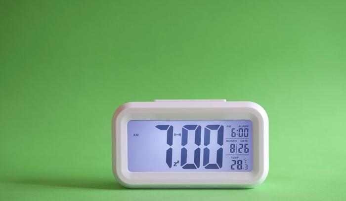 Sveglia digitale sul tavolo con sfondo verde. Visualizzazione delle 7:00 del mattino.