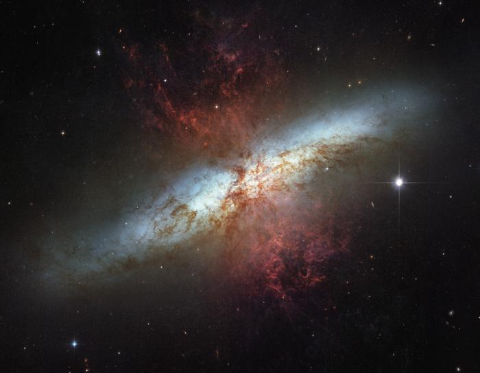 La galassia è disordinata. il suo corpo principale è una regione sfocata bianco-azzurra luminosa. Sopra di essa a novanta gradi è visibile un vetro a forma di ora di polvere rossa e gas