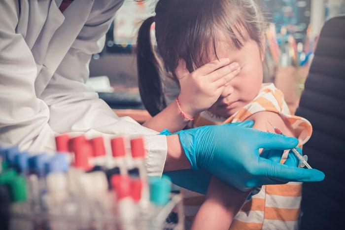 ragazzina si copre gli occhi mentre il medico le inietta un vaccino