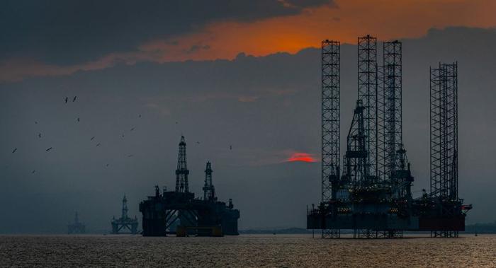 Piattaforme petrolifere offshore in mare contro un tramonto rosso.