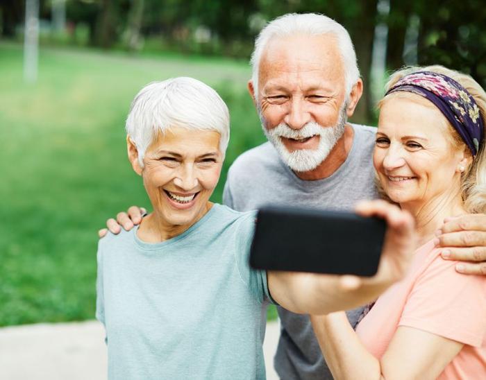 tre persone anziane, due donne e un uomo, sorridenti insieme e scattando un selfie in un parco, indossando abiti da ginnastica