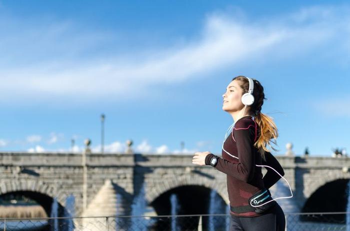 donna in abbigliamento da allenamento con cuffie over-ear che corre lungo il fiume con un ponte sullo sfondo