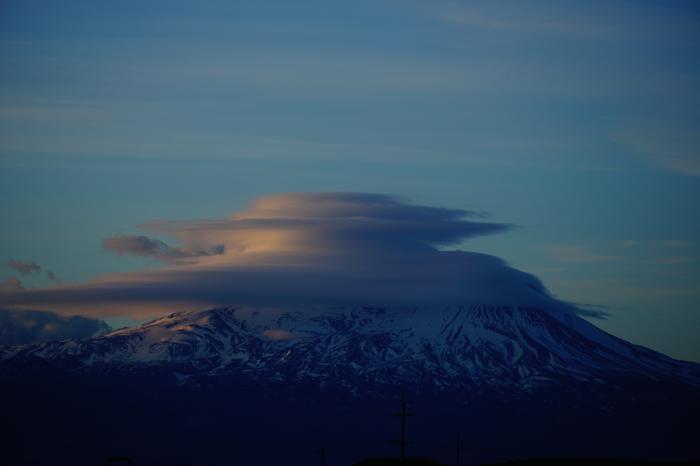 montagna innevata con la cima parzialmente oscurata da una formazione nuvolosa rotonda al tramonto