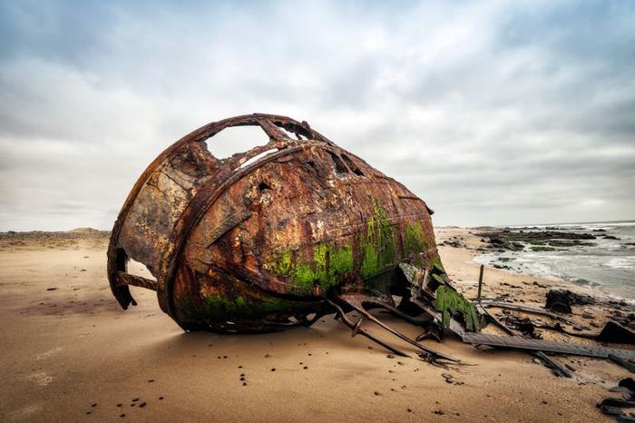 Naufragio lungo la Costa dello Scheletro nell'ovest della Namibia scattato nel gennaio 2018; carcassa di una nave con sentina verde sul fondo sdraiata su un lato su una spiaggia