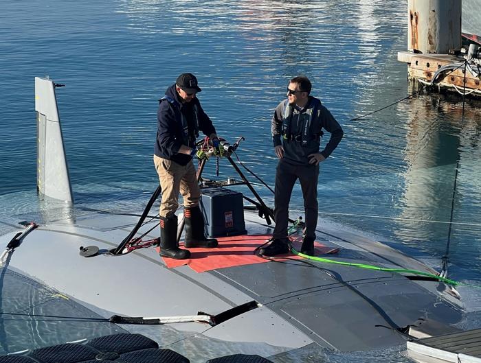 due membri del team del progetto in piedi sulla parte superiore del veicolo Manta Ray mentre galleggia in acqua, indossano giubbotti di salvataggio e lavorano con dell'attrezzatura