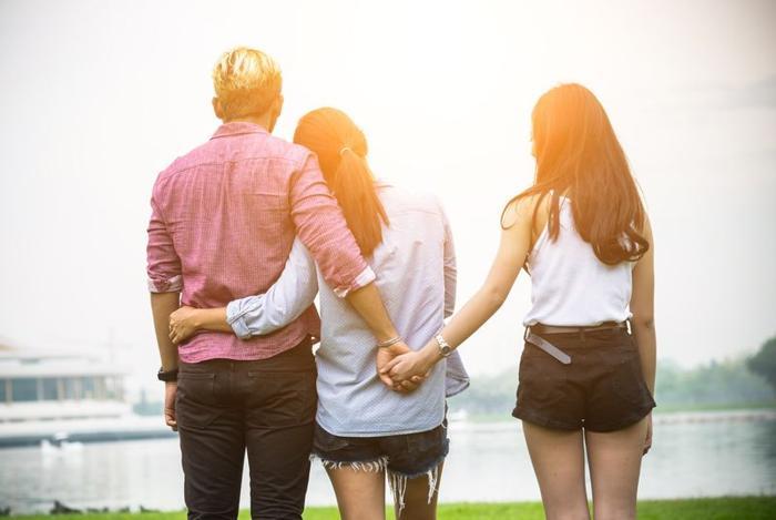 a-couple-with-their-arms-around-each-other-but-the-man-is-holding-hands-with-another-woman-behind-his-partner-s-back-m-2.jpg