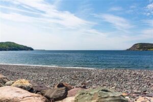 Spiaggia rocciosa con cielo blu e masse terrestri verdi sullo sfondo