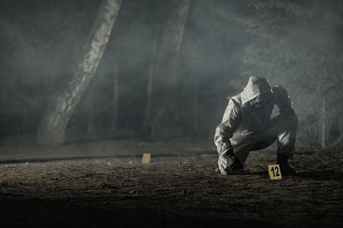 Scienziato forense accovacciato in una scena del crimine in una foresta nebbiosa