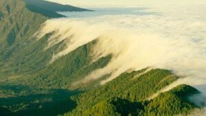 fotografia di un'area montuosa verde che dimostra l'effetto foehn; un lato è soleggiato, l'altro è coperto da nuvole bianche