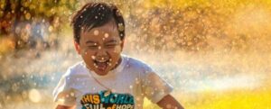 Il bambino corre felicemente attraverso l'irrigatore